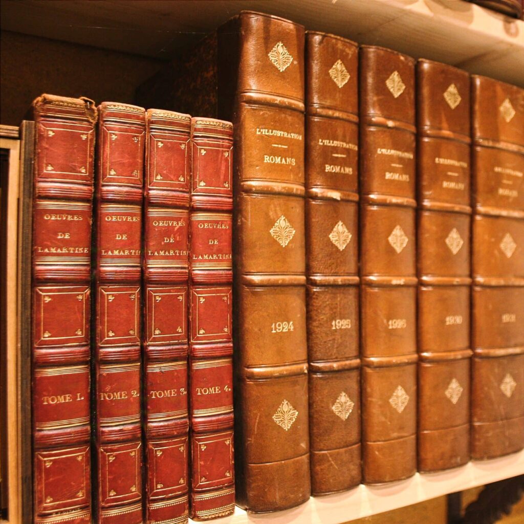 Collection de livres anciens reliés en cuir, alignés sur une étagère en bois, comprenant les œuvres de Lamartine et des volumes de l’Illustration Romans.